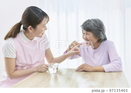 シニア女性の歯磨き指導をする若い歯科衛生士 97135403