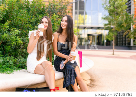 Joyful stylish girlfriends drinking coffee after shopping 97138763