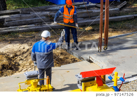 Two workers in construction helmets and overalls laying concrete slab on construction site on summer Two workers in construction helmets and overalls laying concrete slab on construction site on summer 97147526