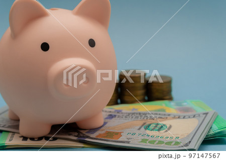 Pink piggy bank and a stack of dollars, euros and coins on a blue background. 97147567