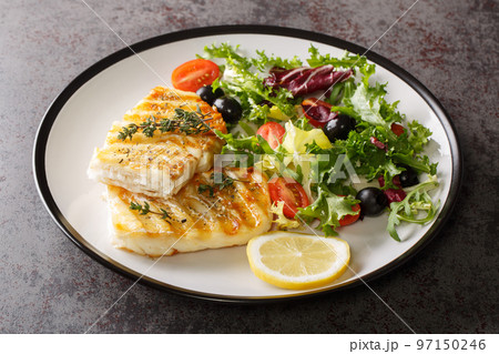 Spicy grilled cod fish fillet with fresh vegetable salad and leaf lettuce mix and lemon close-up in a plate. Horizontal 97150246