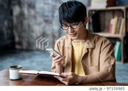 読書中にスマホを使う眼鏡の若い男性 97150965