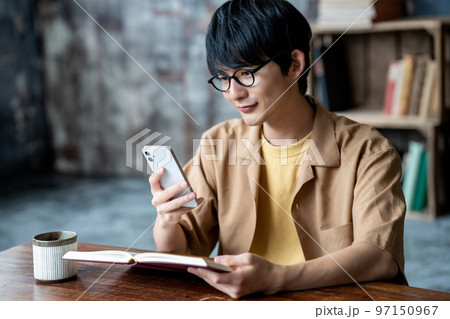 読書中にスマホを使う眼鏡の若い男性 読書中にスマホを使う眼鏡の若い男性 97150967