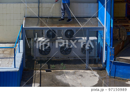 A worker washes cleans the air conditioning system in the backyard of a factory 97150989