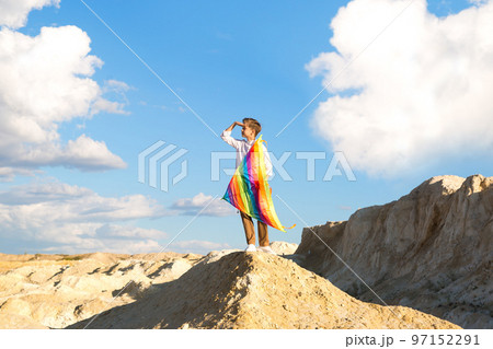 A 9-year-old boy with a bright colorful kite stands high on a mountain against a background of beautiful clouds and looks into the distance 97152291