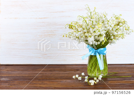 bouquet of lilies of the valley in a vase with blue ribbon on a brown white wooden background bouquet of lilies of the valley in a vase with blue ribbon on a brown white wooden background 97156526