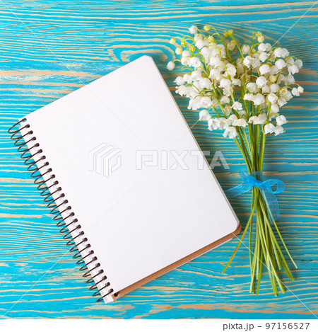 Bouquet of flowers lily of the valley and empty paper notebook on blue rustic table. Bouquet of flowers lily of the valley and empty paper notebook on blue rustic table. 97156527