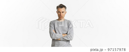 Image of angry middle-aged man feeling offended, cross arms on chest and squinting at camera, standing over white background 97157978