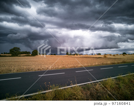 Straight road, crop and dark stormy clouds Straight road, crop and dark stormy clouds 97160841