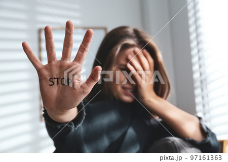 Crying young woman showing palm with word STOP indoors, focus on hand. Domestic violence concept 97161363