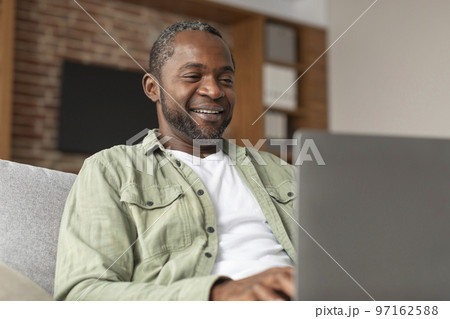 Cheerful mature black man typing on computer, has video call, enjoy communication due social distance Cheerful mature black man typing on computer, has video call, enjoy communication due social distance 97162588