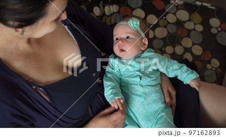Cute baby girl lying on legs of her mother at home. Woman resting with infant child on a couch Cute baby girl lying on legs of her mother at home. Woman resting with infant child on a couch 97162893