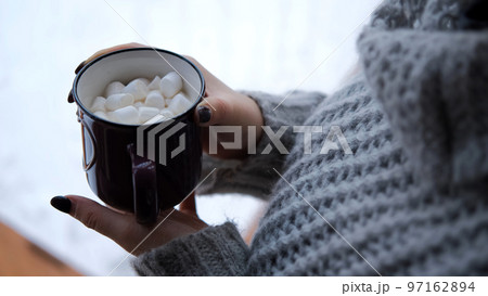 Close-up of young woman in grey knitted sweater drinking tea or hot chocolate with marshmallows on winter holidays 97162894