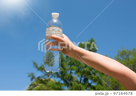 A child's hand is holding a bottle of drinking water against the blue sky A child's hand is holding a bottle of drinking water against the blue sky 97164678