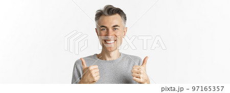 Close-up of cheerful middle-aged man, smiling happy and satisfied, showing thumbs-up, expressing approval, like something good, standing over white background 97165357