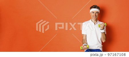 Image of handsome middle-aged male athlete, workout with dumbbells and smiling, training against orange background 97167108