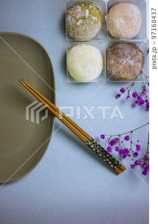 Traditional Japanese dessert mochi in rice dough or daifuku. Mochi ice cream balls and gray plate, food chopsticks on blue background top view. Table setting, violet flowers decor. Selective focus. Traditional Japanese dessert mochi in rice dough or daifuku. Mochi ice cream balls and gray plate, food chopsticks on blue background top view. Table setting, violet flowers decor. Selective focus. 97168437