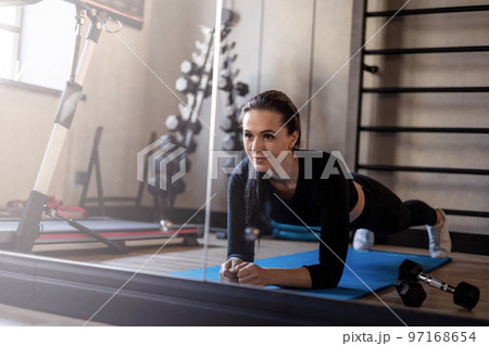 Beauty brunette woman standing in plank position in front of mirror at gym physical activity 97168654