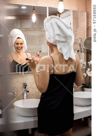 Happy brunette woman applying makeup powder blush foundation use brush in front mirror at bathroom Happy brunette woman applying makeup powder blush foundation use brush in front mirror at bathroom 97168660