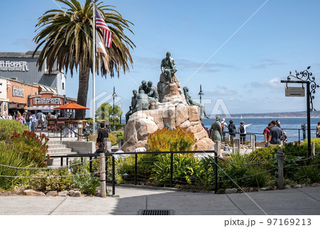 Monterey, USA, September 20, 2022. View of Cannery Row Monument with bronze human sculptures on rocks at coastline of Monterey bay with blue sky in the background during sunny day 97169213