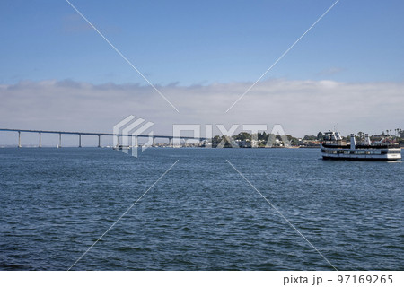 Ship sailing on San Diego bay and distant view of Coronado bridge over seascape with cloudy sky in the background during sunny day Ship sailing on San Diego bay and distant view of Coronado bridge over seascape with cloudy sky in the background during sunny day 97169265