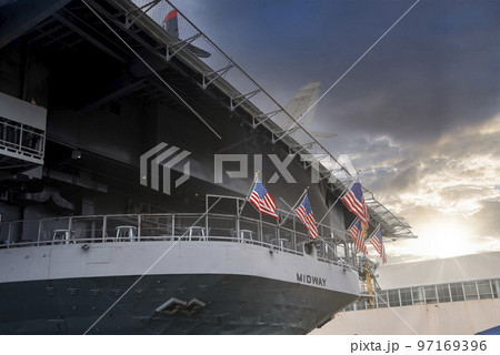 San Diego, USA. September 20, 2022. American flags waving on large USS Midway aircraft carrier below cloudy sky during sunset San Diego, USA. September 20, 2022. American flags waving on large USS Midway aircraft carrier below cloudy sky during sunset 97169396