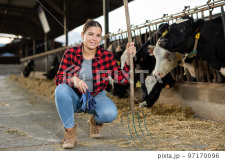 Portrait of positive woman farmer with pitchfork in cowhouse 97170096