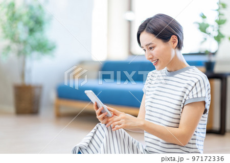 リビングでスマートフォンを操作する女性。 リビングでスマートフォンを操作する女性。 97172336