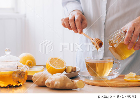 Women's hands prepare hot drink tea from ginger root lemon honey for cold treatment and prevention Women's hands prepare hot drink tea from ginger root lemon honey for cold treatment and prevention 97174041
