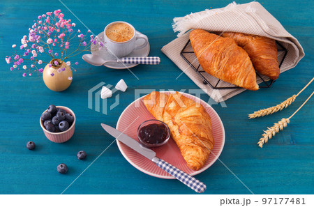 Tasty breakfast with croissants, fresh blueberries, jam and cup of coffee. Blue wooden table, high angle of view, no people. 97177481