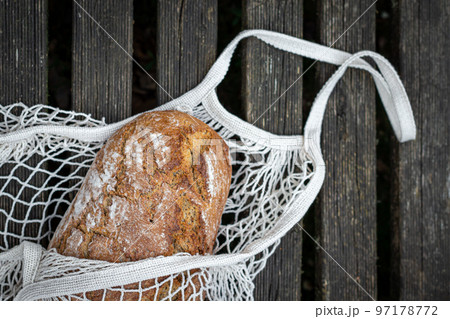 Fresh bread in a shopping bag on a wooden background, flat lay. 97178772