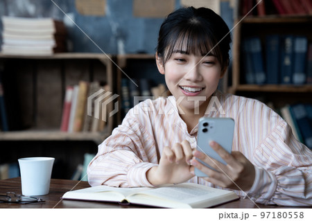 読書中にスマホを操作する若い女性 読書中にスマホを操作する若い女性 97180558