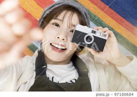 ラグマットに寝転んでフィルムカメラを持つ若い女性 97180684
