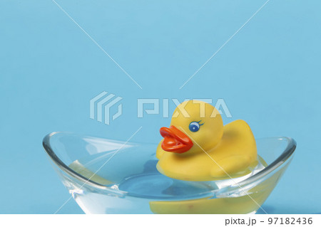 A yellow rubber duck floats in a bath on a blue background. 97182436