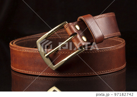 Part of a leather brown belt with a metal buckle on a black background. Part of a leather brown belt with a metal buckle on a black background. 97182742