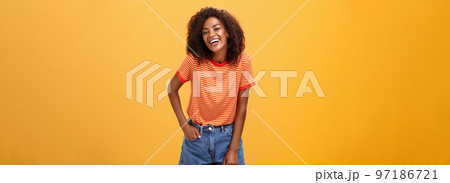 Portrait of charismatic charming african american stylish african american female in trendy shorts and t-shirt laughing happily enjoying talking with cool people laughing posing over orange background 97186721