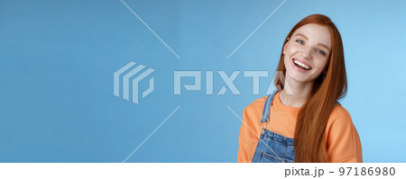 Positive outgoing lively redhead girl laughing joyfully having fun talking friendly friends tilting head chuckling joking funny life moments standing positive lucky blue background orange t-shirt 97186980