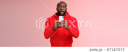 Impressed focused handsome african american bearded guy looking intrigued holding smartphone recording video capturing awesome fight, widen eyes curious surprised, standing pink background 97187072