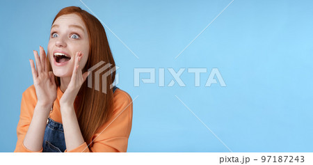 Attractive silly european redhead young girl 20s calling friend searching someone crowd look relaxed joyfully yelling hold hands opened mouth shouting name louder look left, blue background 97187243