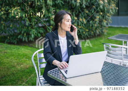 Asian confident business woman talking on phone and working with laptop outdoor. Job, work aspirational concept. Business people lifestyle, copy space 97188352