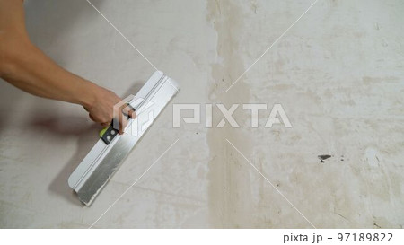 Master's hands apply the finishing putty on the concrete wall, close-up, there is a place for the inscription. Hand with a spatula to apply putty on the wall. 97189822