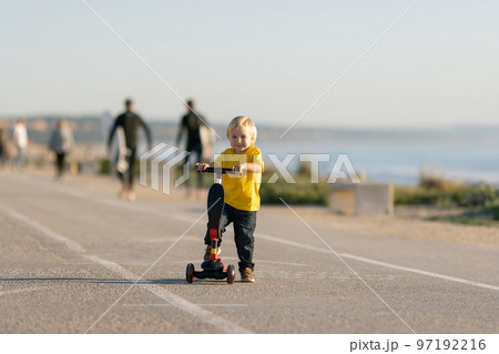 Smiling little boy stands on the road with a scooter Smiling little boy stands on the road with a scooter 97192216
