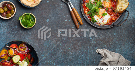 Middle Eastern breakfast or brunch with Shakshouka, toasts, vegetables salad, hummus, olives copy space 97193454