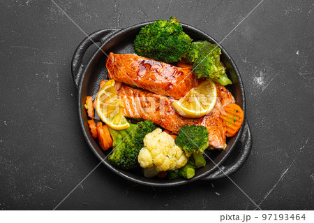 Healthy baked fish salmon steaks, broccoli, cauliflower, carrot in cast iron casserole bowl on black dark stone background. Cooking a delicious low carb dinner, healthy nutrition 97193464