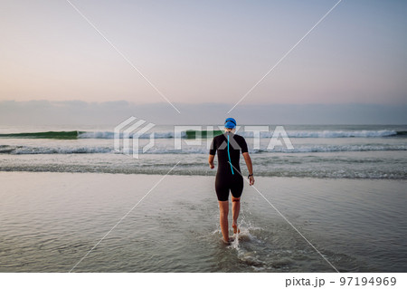 Rear view of woman in neoprene entering in to ocean. 97194969