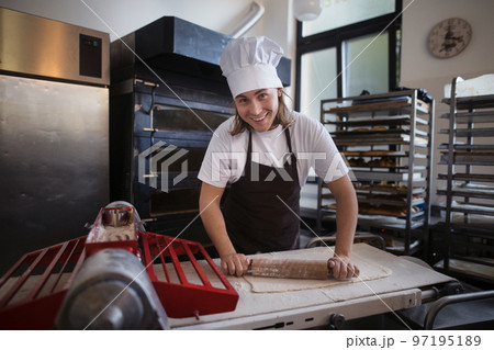 Young baker with chef cap preparing pastries in bakery. Young baker with chef cap preparing pastries in bakery. 97195189
