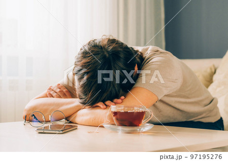 A tired adult woman lies on table with her hand under her head. Woman is going through fatigue reworking 97195276