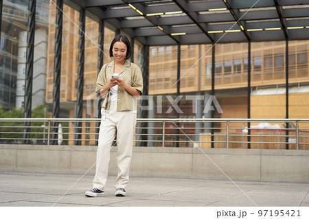 Portrait of asian female model with telephone. Young korean girl holding smartphone on street, using telephone Portrait of asian female model with telephone. Young korean girl holding smartphone on street, using telephone 97195421
