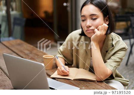 Portrait of young korean girl making notes, listening online meeting, lecture, looking at laptop screen, working remotely from cafe Portrait of young korean girl making notes, listening online meeting, lecture, looking at laptop screen, working remotely from cafe 97195520