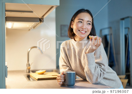 Beautiful young asian woman eating toast on her kitchen, drinking coffee and smiling 97196307